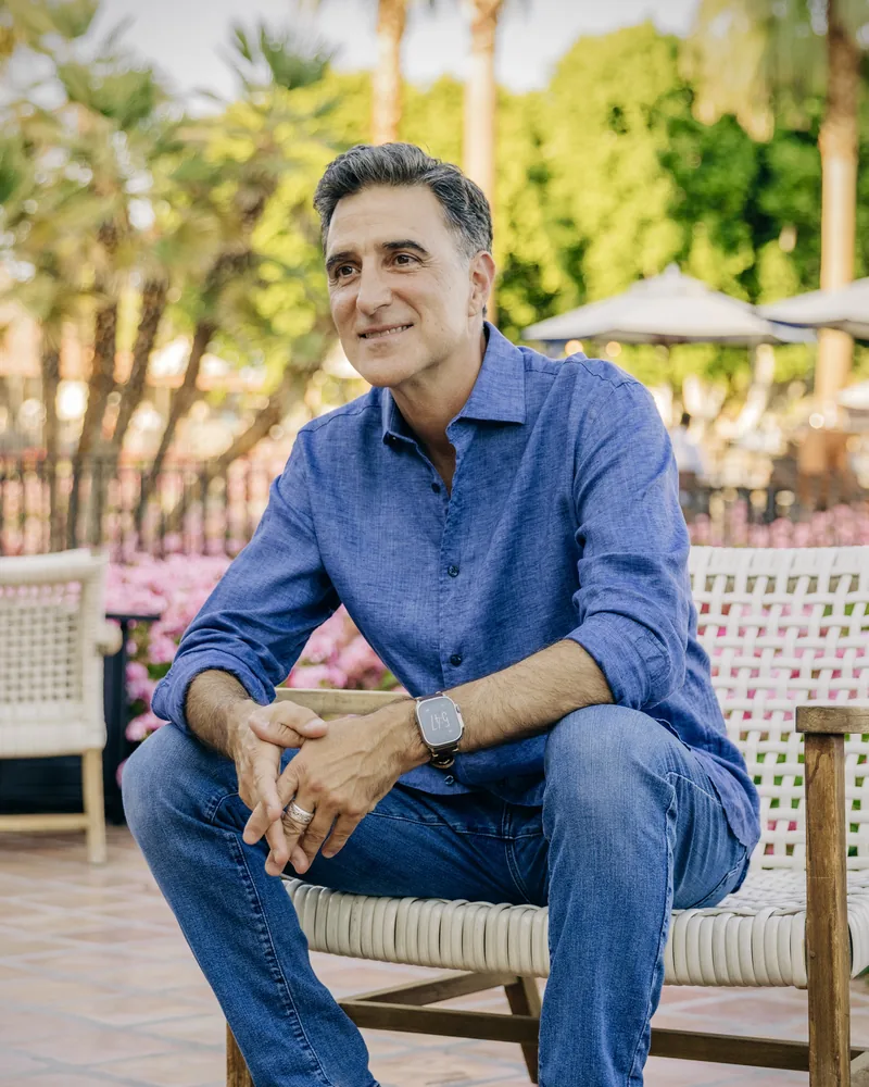 AI communication coach: Salvatore Manzi, smiling, seated outdoors among palm trees in a blue linen shirt